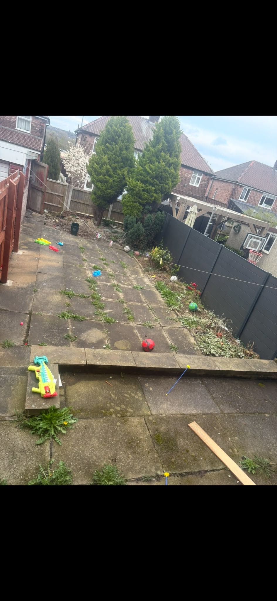 Chadderton garden before work, with old paving, weeds and trees beside the fences