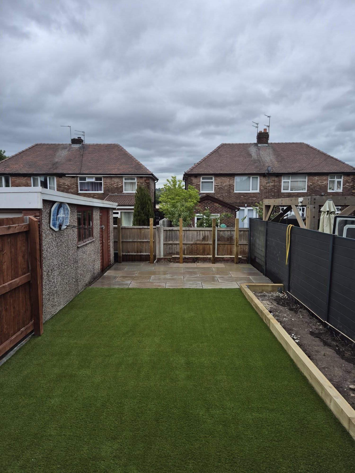 Finished artificial grass installation in Chadderton with paving and a timber-edged planter